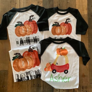 May include: Three black and white baseball shirts with pumpkin designs. The shirts have the names Landon, Boston, and Asher printed on them.