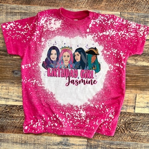 May include: Pink t-shirt with a bleach-splattered design featuring a group of cartoon characters and the text "Birthday Girl Jasmine".