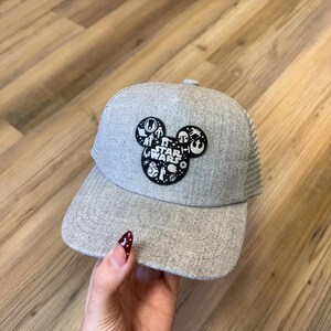 May include: A grey Star Wars baseball cap with a mesh back and a curved peak. The front has a Mickey Mouse head design with Star Wars characters and logos. The cap is made of a textured fabric.