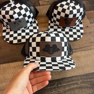K&ouml;nnte beinhalten: Drei schwarz-wei&szlig; karierte Trucker-M&uuml;tzen mit einem Mickey-Mouse-Aufn&auml;her. Die M&uuml;tzen haben einen schwarzen Mesh-R&uuml;cken und einen flachen Schirm. Der Mickey-Mouse-Aufn&auml;her ist braun, grau und schwarz.