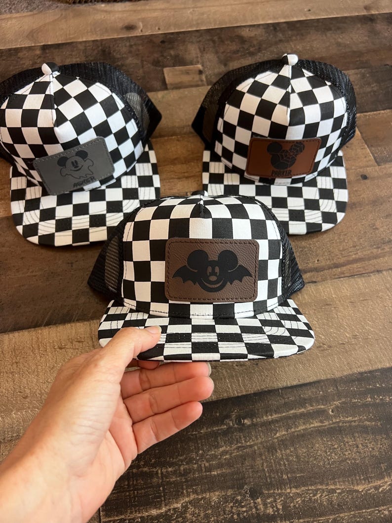 K&ouml;nnte beinhalten: Drei schwarz-wei&szlig; karierte Trucker-M&uuml;tzen mit einem Mickey-Mouse-Aufn&auml;her. Die M&uuml;tzen haben einen schwarzen Mesh-R&uuml;cken und einen flachen Schirm. Der Mickey-Mouse-Aufn&auml;her ist braun, grau und schwarz.