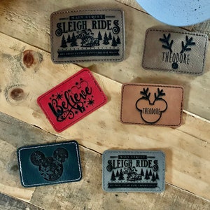 May include: Six different Christmas-themed iron-on patches. The patches are made of faux leather and feature various designs, including a sleigh ride, a reindeer, a Mickey Mouse head, and the word "Believe".