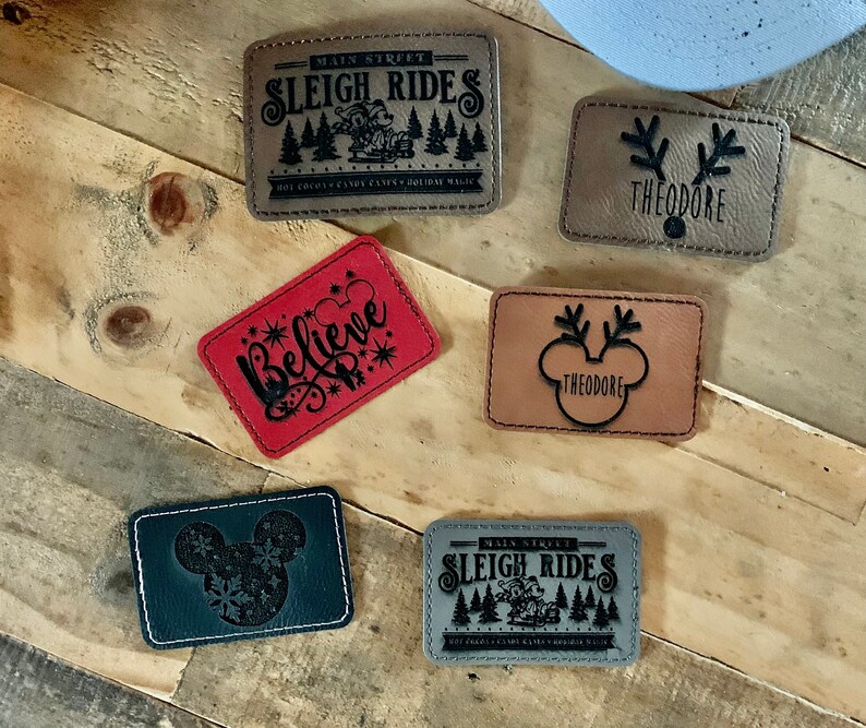 May include: Six different Christmas-themed iron-on patches. The patches are made of faux leather and feature various designs, including a sleigh ride, a reindeer, a Mickey Mouse head, and the word "Believe".