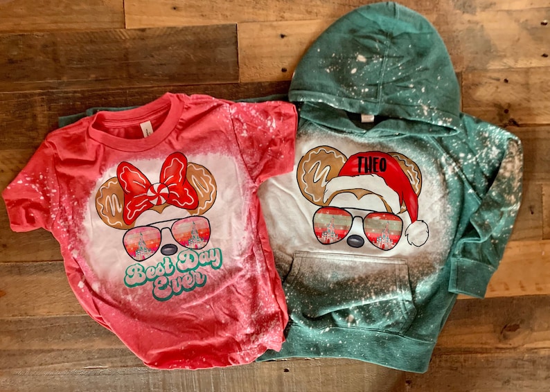 May include: Two bleached shirts with a Christmas Mickey Mouse design. One shirt is red with the text "Best Day Ever" and the other is green with the name "Theo".