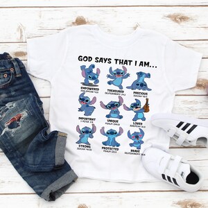 May include: White t-shirt with a blue cartoon character, Stitch, in different poses. Each pose has a bible verse and a word describing Stitch, such as "empowered", "treasured", "precious", "important", "unique", "loved", "strong", "protected", and "brave". The text "GOD SAYS THAT I AM..." is at the top of the shirt.