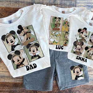 May include: White t-shirts with a Mickey Mouse design featuring different poses of Mickey Mouse in a safari setting. The shirts have the names "Dad", "Emma", and "Luc" printed on them.