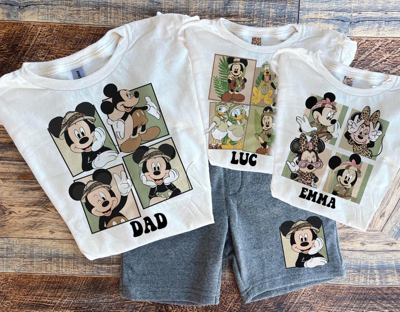 May include: White t-shirts with a Mickey Mouse design featuring different poses of Mickey Mouse in a safari setting. The shirts have the names "Dad", "Emma", and "Luc" printed on them.