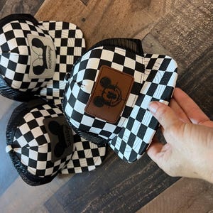 K&ouml;nnte beinhalten: Schwarz-wei&szlig; karierte Trucker-H&uuml;te mit Mesh-R&uuml;cken. Ein Hut hat einen braunen Aufn&auml;her mit einem Mickey-Mouse-Design, ein anderer hat einen grauen Aufn&auml;her mit dem Wort "Mommy". Der dritte Hut hat einen grauen Aufn&auml;her mit dem Wort "Daddy".