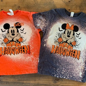 Puede incluir: Dos camisetas salpicadas de lej&iacute;a con un dise&ntilde;o de Mickey Mouse y Minnie Mouse de Halloween. La camiseta naranja dice "LUCAS HALLOWEEN" y la camiseta azul oscuro dice "HALLOWEEN".