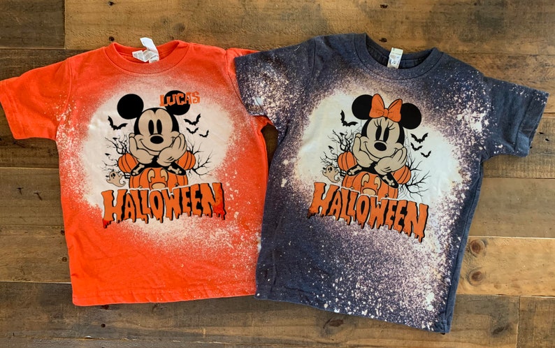 Puede incluir: Dos camisetas salpicadas de lej&iacute;a con un dise&ntilde;o de Mickey Mouse y Minnie Mouse de Halloween. La camiseta naranja dice "LUCAS HALLOWEEN" y la camiseta azul oscuro dice "HALLOWEEN".