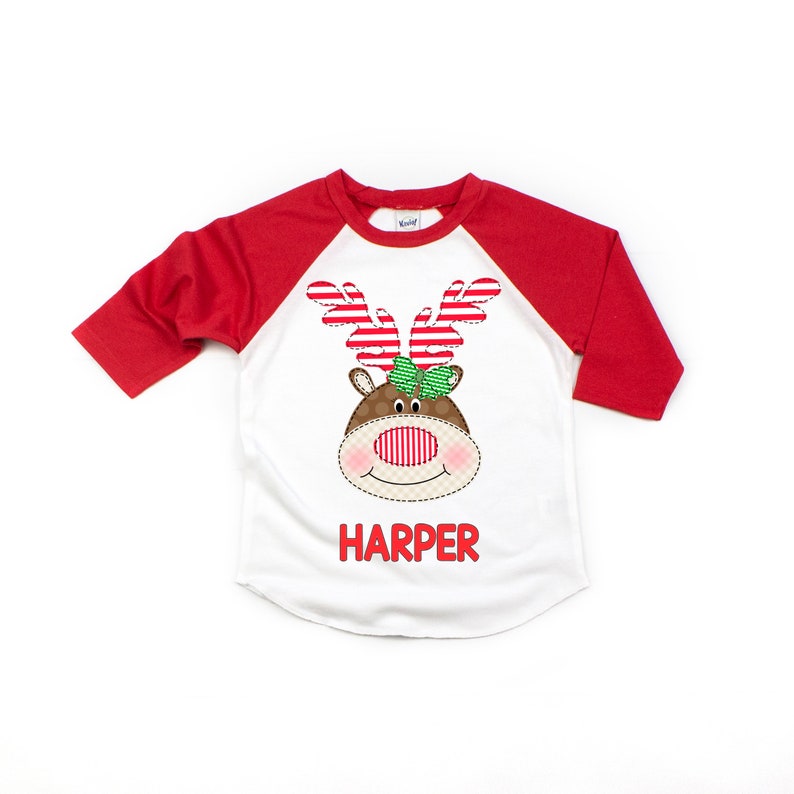 May include: White and red raglan t-shirt with a brown reindeer face graphic and the name "HARPER" printed on the front.