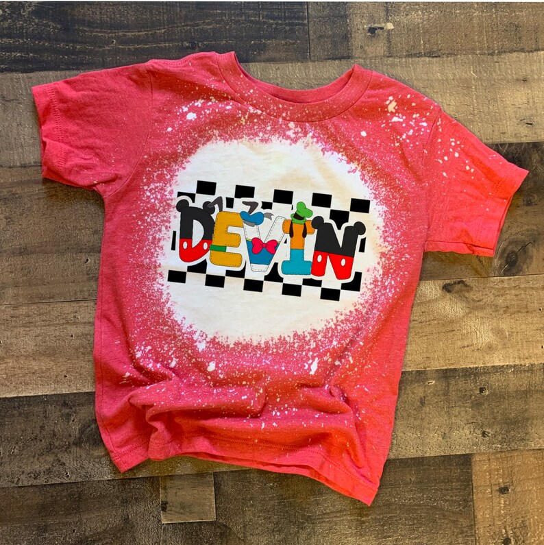 May include: Red t-shirt with a bleach-splattered design featuring a checkered background and the name "DEVIN" in white letters with Disney characters incorporated into the letters.