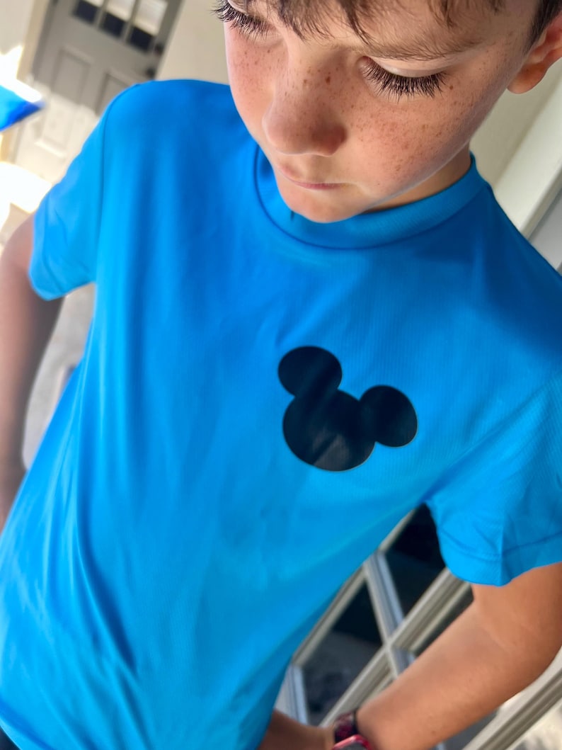 May include: Bright blue t-shirt featuring a black Mickey Mouse silhouette on the chest. The shirt has short sleeves and a crew neck. The fabric appears to be a lightweight, breathable material.