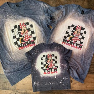 May include: Three blue, white, and red bleached t-shirts with a cartoon image of Minnie Mouse in a checkered pattern. The shirts are personalized with the names "Nana", "Asalta", and "Isla".