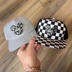 May include: Two baseball caps with a Star Wars theme. One is grey with a mesh back and a Mickey Mouse-shaped patch. The other is black and white chequered with a mesh back and a similar patch. Both patches feature Star Wars characters.