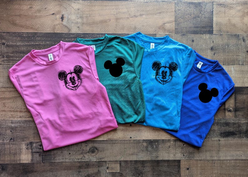 May include: Four colorful t-shirts: pink, teal, blue, and royal blue. Each shirt features a Mickey Mouse graphic or silhouette. The Mickey Mouse graphic is a black sketch, while the silhouette is solid black.