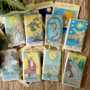 May include: A set of 10 tarot cards, each featuring a different image and text. The cards are printed on a white background with colorful illustrations. The cards are arranged in a semi-circle on a brown surface. The cards include The Fool, The Sun, Temperance, The Magician, The Moon, The World, The Star, The Empress, and Ace of Cups.
