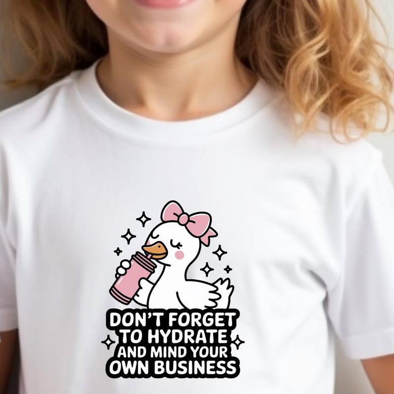 May include: White t-shirt featuring a cartoon duck with a pink bow, holding a pink water bottle. The text reads "DON'T FORGET TO HYDRATE AND MIND YOUR OWN BUSINESS". The design includes stars and is suitable for kids.