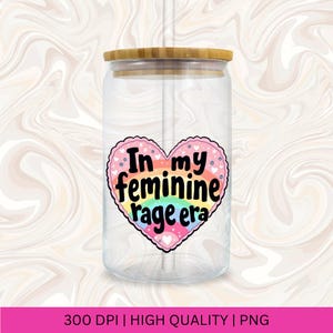 May include: A clear glass jar with a bamboo lid and a straw. The jar has a pink heart sticker with the text "In my feminine rage era" in black lettering. The heart sticker has a rainbow design.