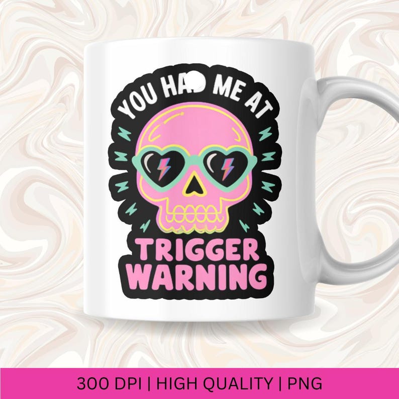 Pu&ograve; includere: Tazza in ceramica bianca con un disegno di teschio rosa che indossa occhiali da sole a forma di cuore con dettagli a fulmine. La tazza ha il testo "YOU HAD ME AT TRIGGER WARNING" in nero e rosa. La tazza ha un manico bianco.