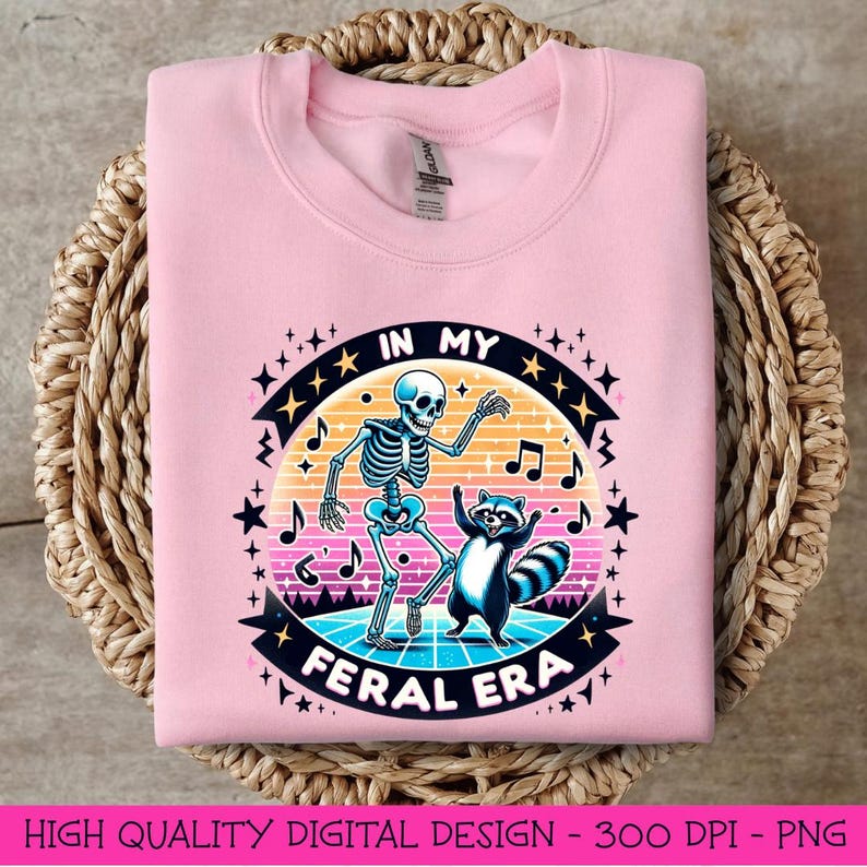 May include: Pink sweatshirt featuring a graphic design of a skeleton and a raccoon dancing with the text "In My Feral Era" in a retro style.