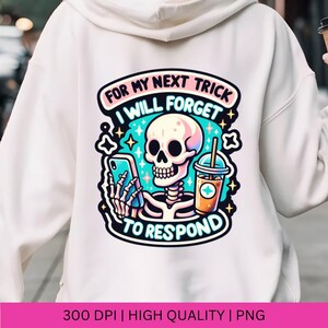 May include: A white hoodie with a colorful graphic design featuring a skeleton holding a phone and a cup of iced coffee. The text reads "For my next trick I will forget to respond".