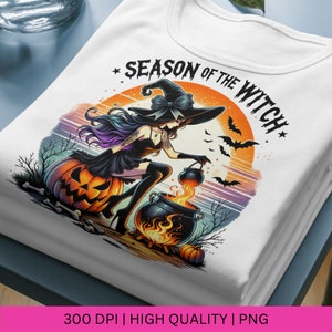 May include: A white t-shirt featuring a colourful illustration of a witch stirring a cauldron against a sunset backdrop. The text "Season of the Witch" is written in a stylised font above the witch.