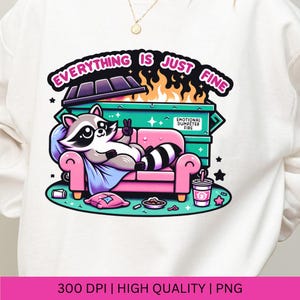 May include: A white sweatshirt with a graphic design of a raccoon sitting on a pink couch in front of a green dumpster with flames coming out of it. The text "Everything is just fine" is above the dumpster and the text "Emotional Dumpster Fire" is on the side of the dumpster.