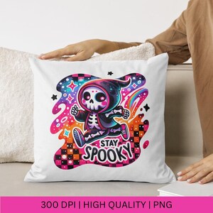 May include: White throw pillow featuring a colourful graphic of a skeleton wearing a hooded cloak and running. The graphic includes a rainbow and stars. The text "Stay Spooky" is below the skeleton.