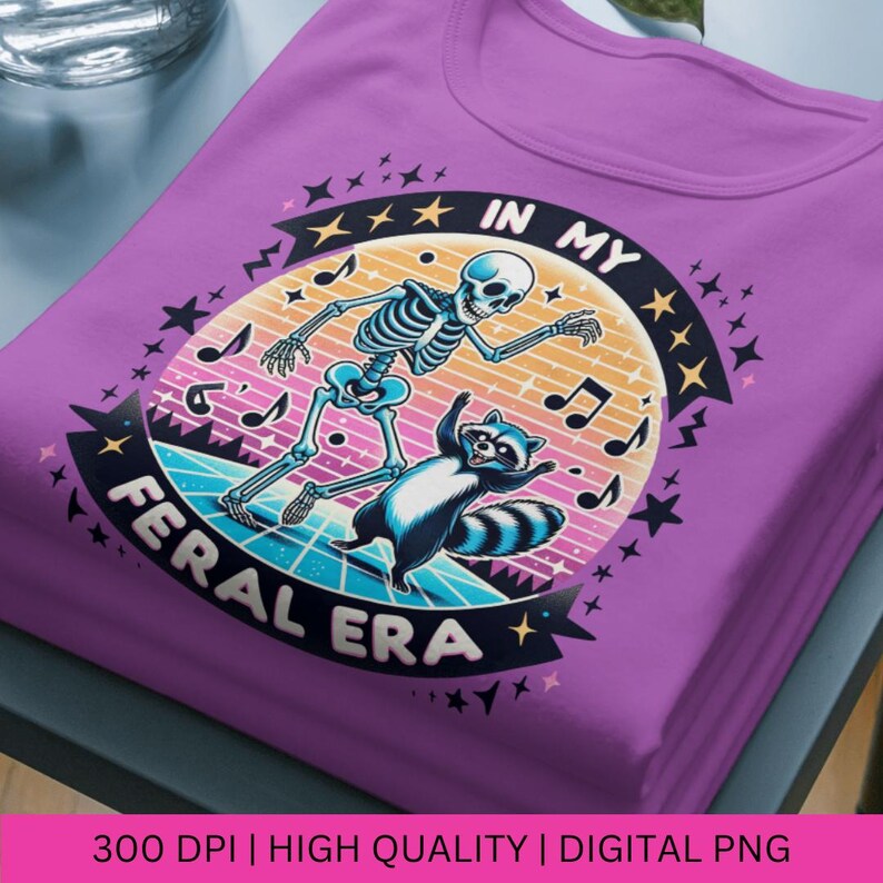 May include: A purple t-shirt featuring a graphic of a skeleton and a raccoon dancing. The graphic is surrounded by stars and musical notes. The text "In My Feral Era" is written in a retro font.