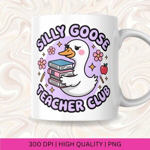 Op de afbeelding: Witte keramische mok met een cartoon gans die boeken vasthoudt, met de tekst "Silly Goose Teacher Club" in paars en wit. Het ontwerp bevat bloemen, sterren, een appel en potloden.