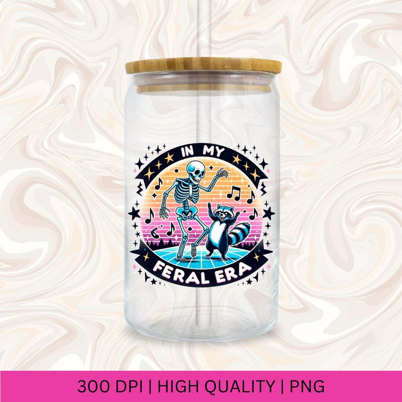 May include: A clear glass tumbler with a bamboo lid and a straw. The tumbler features a colourful graphic of a skeleton and a raccoon dancing with the text "In My Feral Era".