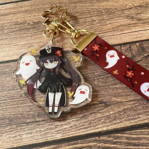 Puede incluir: Un llavero de acrílico transparente con un personaje de anime con cabello negro, un atuendo negro y un sombrero negro. El personaje está rodeado de fantasmas blancos con caras sonrientes. El llavero está unido a una cinta roja con fantasmas blancos y flores rojas impresas.