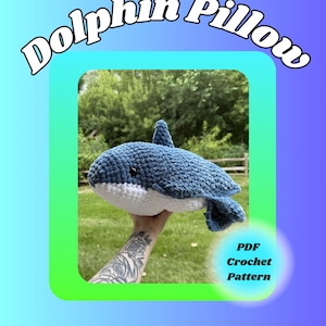 May include: A blue and white crocheted dolphin pillow with a textured yarn finish and black eyes. The image features the text Dolphin Pillow and PDF Crochet Pattern. The design is a soft, stuffed aquatic animal shape with a dorsal fin and tail.