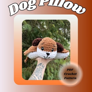 Op de afbeelding: Een gehaakt hondenkussen in bruin en wit met donkerbruine oren en zwarte ogen. De tekst Dog Pillow staat bovenaan en de tekst PDF Crochet Pattern staat rechtsonder. Het pluche speelgoed heeft een zachte, getextureerde garen afwerking.