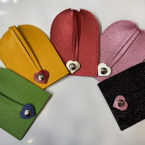 May include: Five leather keychains in different colors, each with a heart-shaped metal charm. The keychains are yellow, red, pink, green, and black.