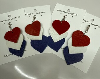 May include: Four leather heart keychains in red, white, and blue. Each keychain has a silver metal ring and a small silver charm. The keychains are displayed on white cards with the text "Handcut Leather" printed on them.
