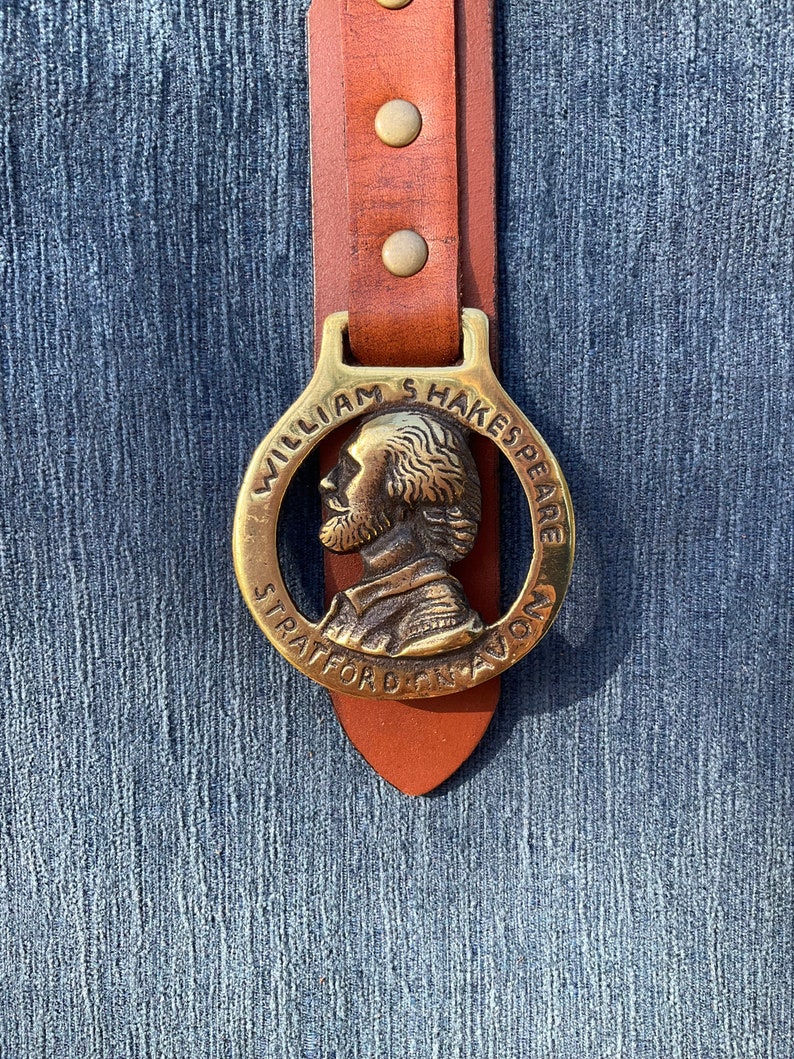May include: A brass belt buckle with a portrait of William Shakespeare and the text "William Shakespeare Stratford Upon Avon".