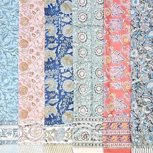 May include: A collection of colorful fabric panels with floral and paisley patterns. The panels feature shades of blue, pink, green, and coral, with intricate designs and decorative borders. The fabrics are likely used for textiles or home decor.