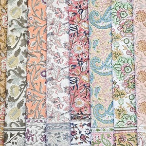 Peut inclure: Plusieurs rouleaux de tissu pliés avec divers motifs floraux et cachemire. La palette de couleurs comprend le pêche, le rose, le bleu, le vert et le beige. Chaque rouleau présente un motif de bordure distinct, mettant en valeur les motifs textiles.