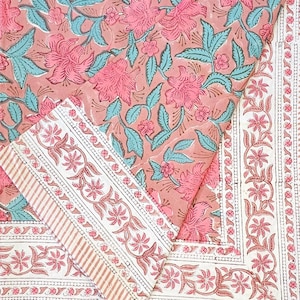 Peut inclure: Textile à motifs floraux avec de grandes fleurs roses, des feuilles turquoise et un fond pêche. Le motif comprend une bordure avec des motifs floraux et rayés. Il s'agit probablement d'une nappe ou d'un tissu.