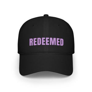 Puede incluir: Gorra de béisbol negra con la palabra "REDEEMED" en letras lavanda en la parte delantera. La gorra tiene una visera curva y una corona estructurada. Un accesorio sencillo y elegante.