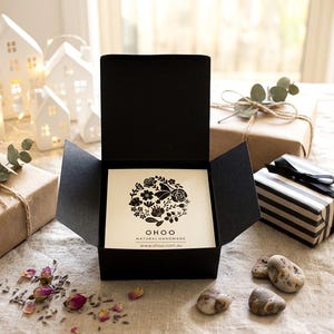May include: A black square gift box with an open lid containing a white card. The card features a circular black floral illustration with the text OHOO NATURAL HANDMADE and the website www.ohoo.com.au printed in black ink at the bottom center.
