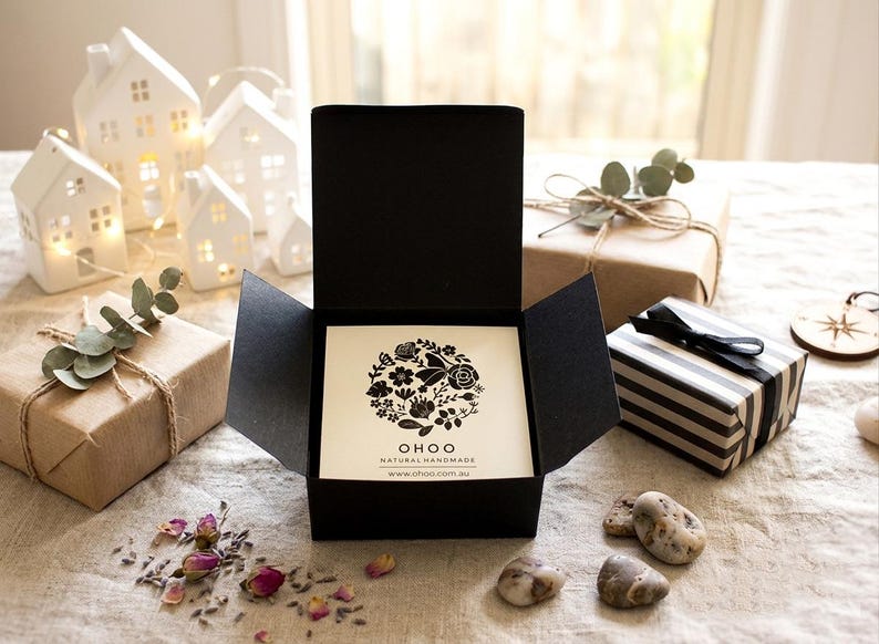 May include: A black square gift box with an open lid containing a white card. The card features a circular black floral illustration with the text OHOO NATURAL HANDMADE and the website www.ohoo.com.au printed in black ink at the bottom center.