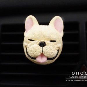 May include: A cream-colored French bulldog head ornament with pink inner ears and tongue, black nose and mouth, and closed eyes. The text OHOO NATURAL HANDMADE CANDLE, ORNAMENT, DIFFUSER is printed in white in the bottom right corner of the image.