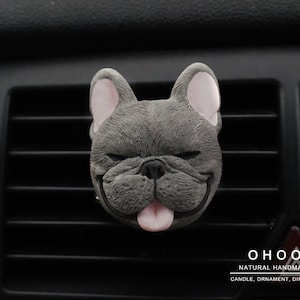 May include: A gray French bulldog head ornament with closed eyes and a pink tongue sticking out. The text OHOO NATURAL HANDMADE CANDLE, ORNAMENT, DIFFUSER is printed in white in the bottom right corner of the image.