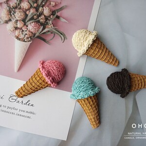 May include: Four handmade ice cream cone ornaments with different coloured scoops: pink, blue, vanilla, and chocolate. The cones are brown, and the scoops have a textured appearance. The image also includes text that reads "Seerei Garden" and "OHOO NATURAL HANDMADE CANDLE, ORNAMENT, DIFFUSER."