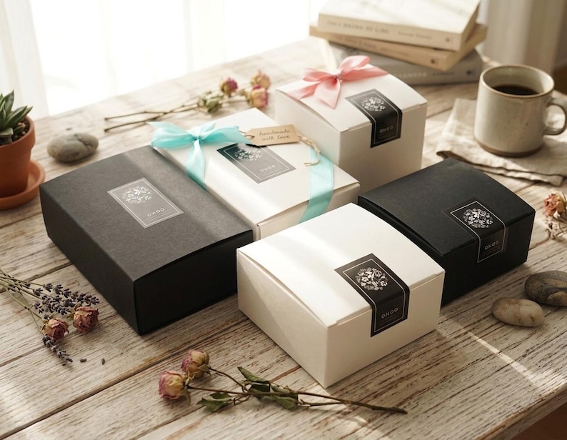 May include: A collection of rectangular and square gift boxes in matte black and white finishes. Each box features a black rectangular label with a white floral graphic and the text ONOO. Some boxes are adorned with light blue or pink satin ribbons.