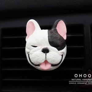 May include: A French bulldog head car air freshener ornament featuring a black and white face with pink ears and tongue, closed eyes, and a smiling expression. The text OHOO NATURAL HANDMADE CANDLE, ORNAMENT, DIFFUSER is printed in the bottom right corner.