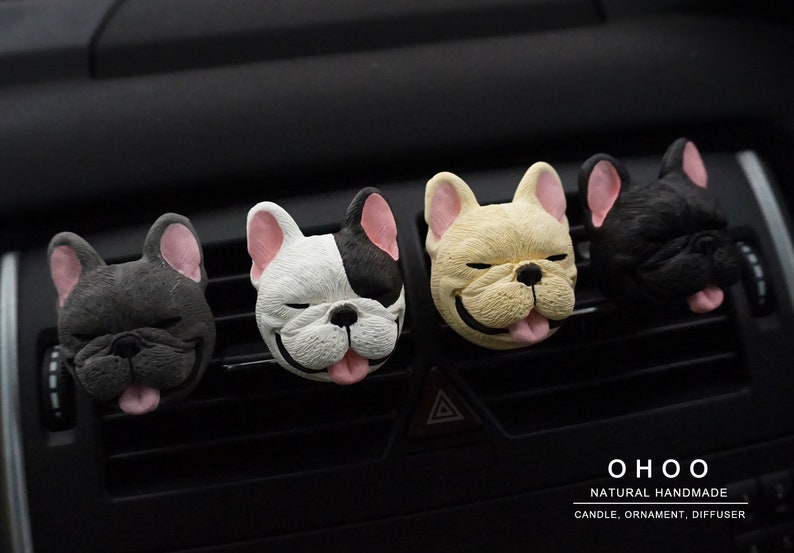 May include: Four French bulldog head ornaments in dark gray, white and black, cream, and black colors, each with pink ears and a tongue sticking out. The text O H O O NATURAL HANDMADE CANDLE, ORNAMENT, DIFFUSER is printed in the bottom right corner.